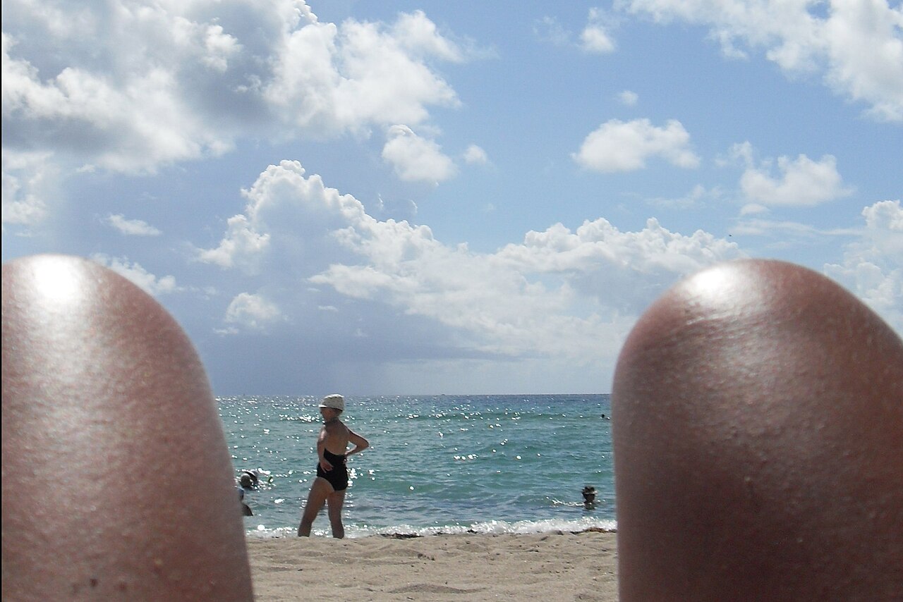 Woman with sleek, humidity-proof hair walking on a sunny Miami beach, looking refreshed.